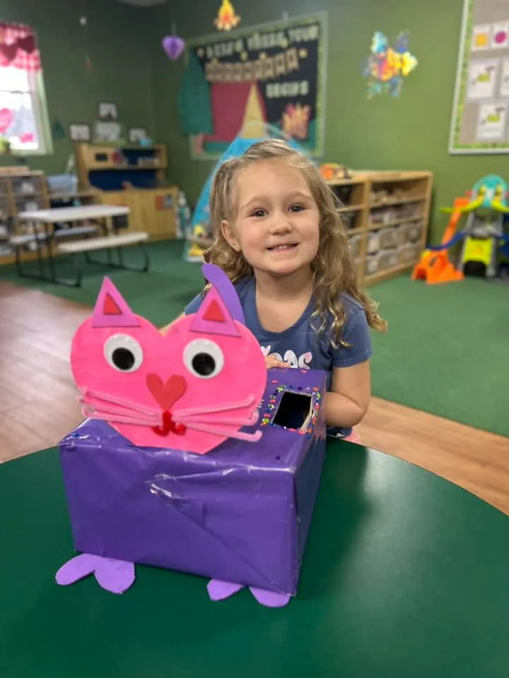 A child smiles behind a toy at Playhouse Children's Center